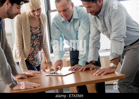 Four people, three man and a woman leaning over a digital tablet on a table. Stock Photo