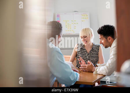 Three business colleagues in an office talking around a table and looking at a digital tablet. Stock Photo