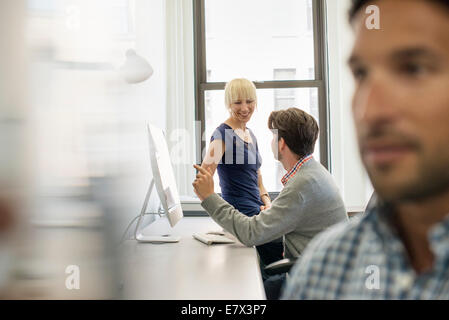 Three business colleagues in an office, two talking and one standing by the door listening. Stock Photo