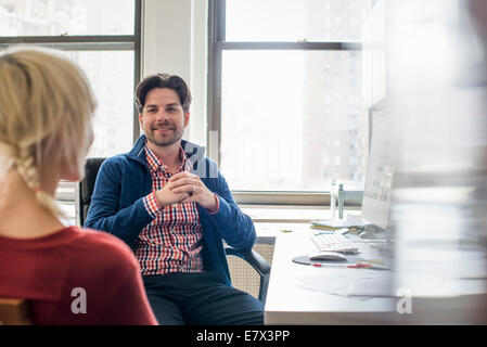 Office life. A man and woman in an office, seated talking to each other. Stock Photo