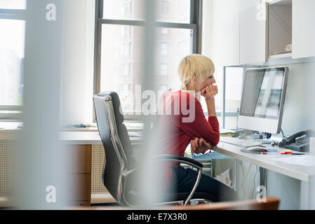 Office life. A woman sitting at a desk using a computer, looking intently at the screen. Stock Photo