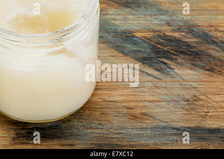 glass jar of coconut cooking oil on grunge wood surface, copy space Stock Photo