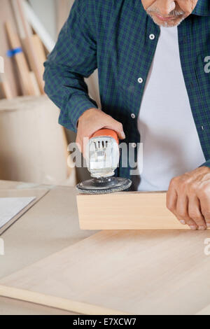 Senior Carpenter Using Electric Sander On Wood Stock Photo