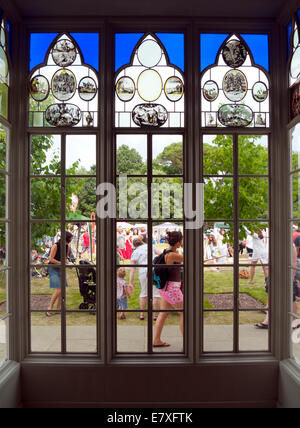 Garden Party Festival at Strawberry Hill House looking out of a stained glass window onto garden & people outside Twickenham in London UK KATHY DEWITT Stock Photo