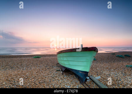 Beautiful sunrise over a green wooden fishing boat on a deserted beach