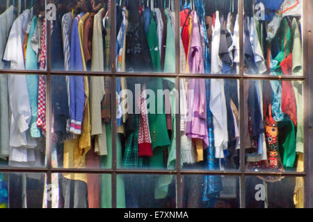 Used clothing on hangers displayed in a thrift store window Stock Photo