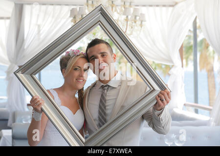 Bride and groom holding a picture frame in front of them and looking through it, photo shoot Stock Photo