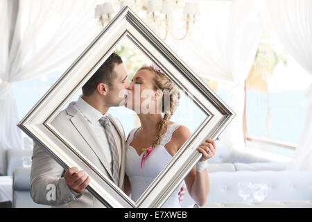 Bride and groom holding a picture frame in front of them, kissing, photo shoot Stock Photo