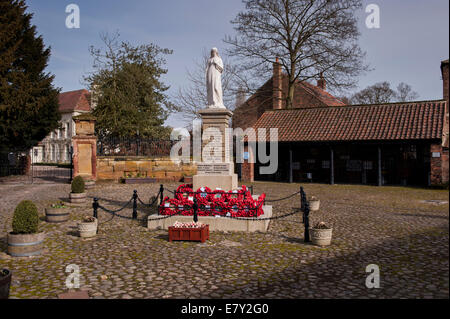 Red poppy wreaths laid at base of war memorial in centre of attractive rural town - cobbled Hall Square, Boroughbridge, North Yorkshire, England, UK. Stock Photo