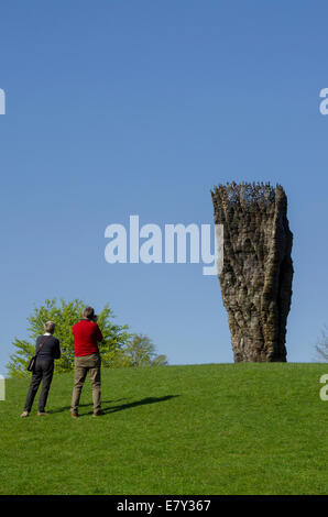 Couple view & photograph tall outdoor sculpture, 'Bronze Bowl with Lace' by Ursula von Rydingsvard & blue sky - Yorkshire Sculpture Park, England, UK. Stock Photo
