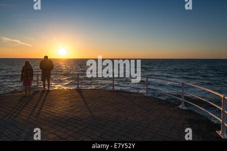 Two silhouetted  people looking to a westerly setting sun on Aberystwyth seafront. Stock Photo