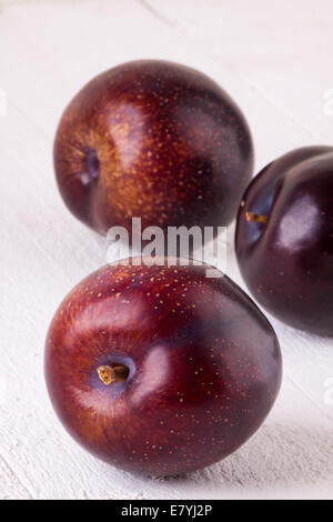 Fresh ripe red juicy appetizing plum close up view with the stalk facing the camera in a concept of healthy eating and diet with two more behind Stock Photo