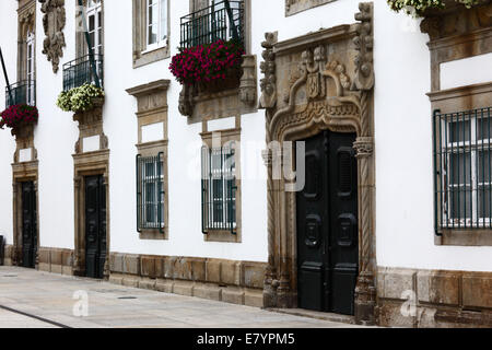 Ornate carved stone doorway and windows of facade of Casa de Carreira mansion with geraniums in window box, Viana do Castelo , northern Portugal Stock Photo