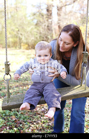 Mother with son (12-23 months) playing on swing in park Stock Photo