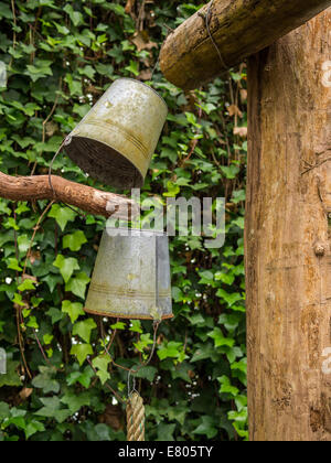 Two old rusty buckets hanging upside down from wooden pole Stock Photo