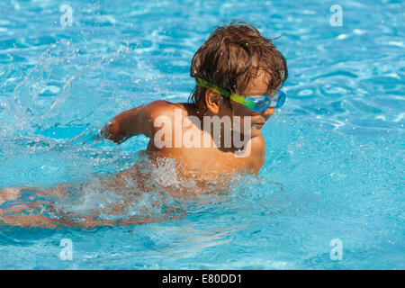 Small boy with water sport goggles swims in pool