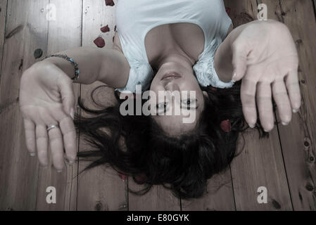 Woman lying on floorboards with her hands raised Stock Photo