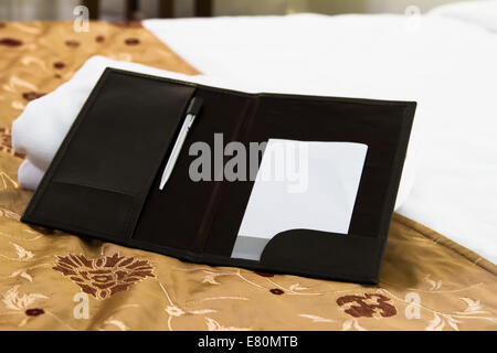 White blank note with pen on bed in hotel room. Stock Photo