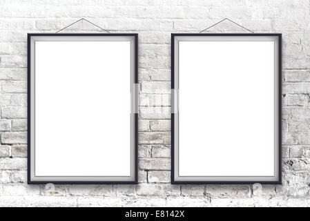 Two blank vertical painting poster in black frame hanging on white brick wall. Stock Photo