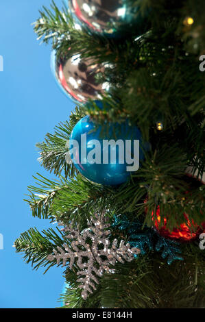 Vertical close up of brightly coloured ornamental Christmas decorations on the real pine tree outside in the sunsh Stock Photo