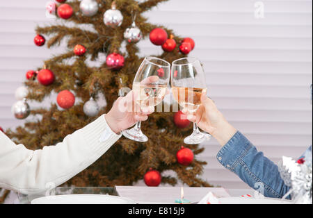 Romantic couple hands holding glasses of champagne and doing clink against Christmas tree.