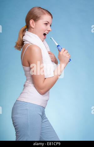 Young woman funny girl singing to toothbrush brushing her white teeth doing fun on blue. Daily dental care. Studio shot. Stock Photo