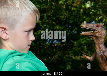 Portrait of child boy playing with toy dinosaur raptor outside Stock Photo