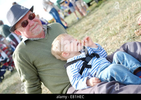 Two year old boy eating an ice cream whilst sitting with his granddad Stock Photo