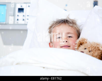 Composite image of sick adorable little boy lying in a hospital bed with his teddy bear Stock Photo