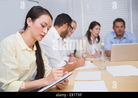 Woman taking notes while colleagues are talking behind her Stock Photo