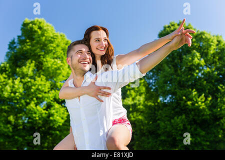 Man carrying woman piggyback in park Stock Photo