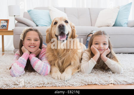 Sisters lying on rug with golden retriever smiling at camera Stock Photo