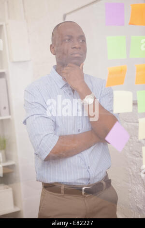 Thoughtful businessman looking at sticky notes on window Stock Photo
