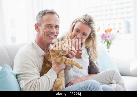 Smiling couple petting their gringer cat on the couch Stock Photo