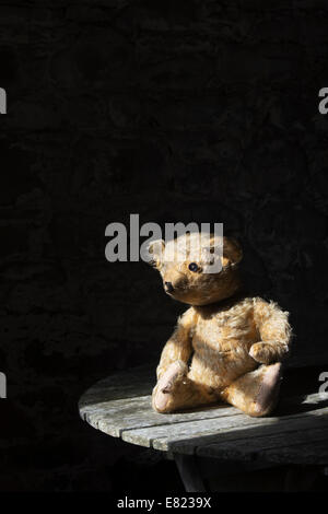 Old Threadbare One Eyed Teddy bear sat on a wooden table in sunlight Stock Photo