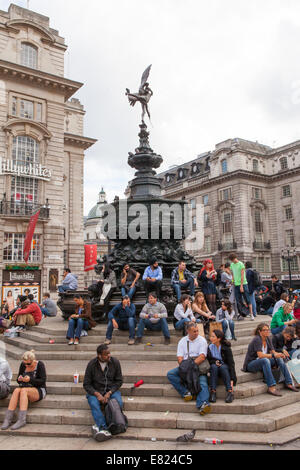Tourists sit and rest on the stairs of one of Piccadilly circus monuments. Stock Photo