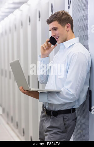 Smiling technician phoning and using his notebook Stock Photo