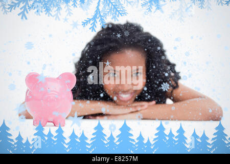 A smiling girl resting her head on her hands with a piggy bank in front of her Stock Photo