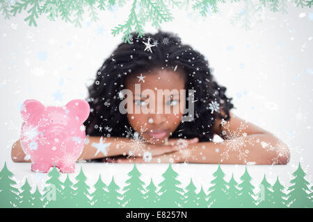 Young woman lying down resting her head on her hands is looking at a piggy bank Stock Photo