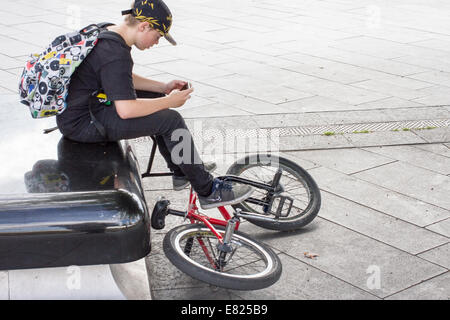 A young teenager looks at a smartphone while sitting with his bike In Sheffield UK Stock Photo
