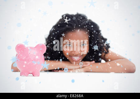 A smiling girl resting her head on her hands with a piggy bank in front of her Stock Photo