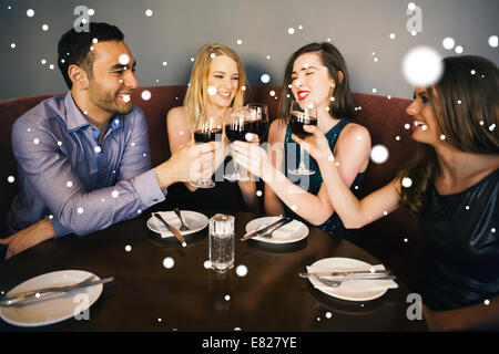 Composite image of laughing friends sitting together clinking glasses Stock Photo