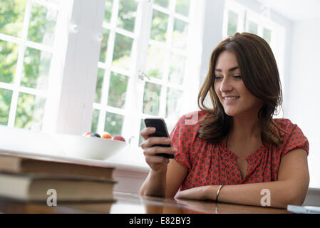 A woman seated at a table, checking her smart phone. Stock Photo