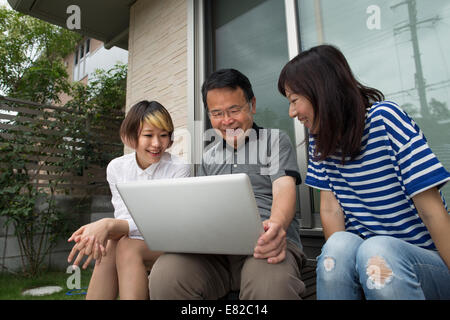 A man and two women sitting outside a house. Holding a laptop computer. Stock Photo