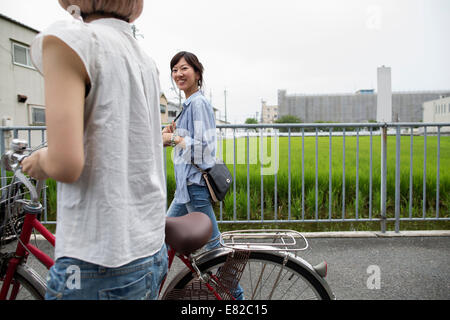Two women walking along a footpath, pushing a bicycle.