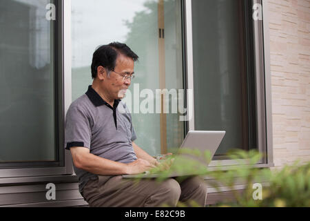 A man sitting outside a house. Holding a laptop computer. Stock Photo