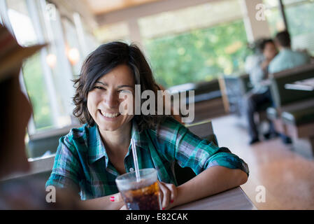 A woman seated holding a cold drink at a diner table. Stock Photo