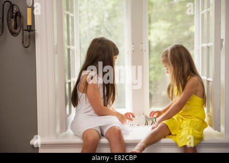 Two girls playing together, sitting on a window seat indoors. Stock Photo