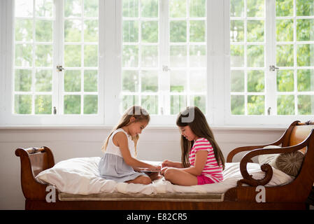 Two girls sitting and playing, using a digital tablet. Stock Photo