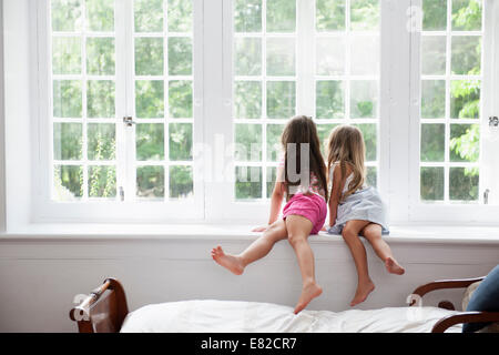 Two girls sitting side by side by a large window. Stock Photo